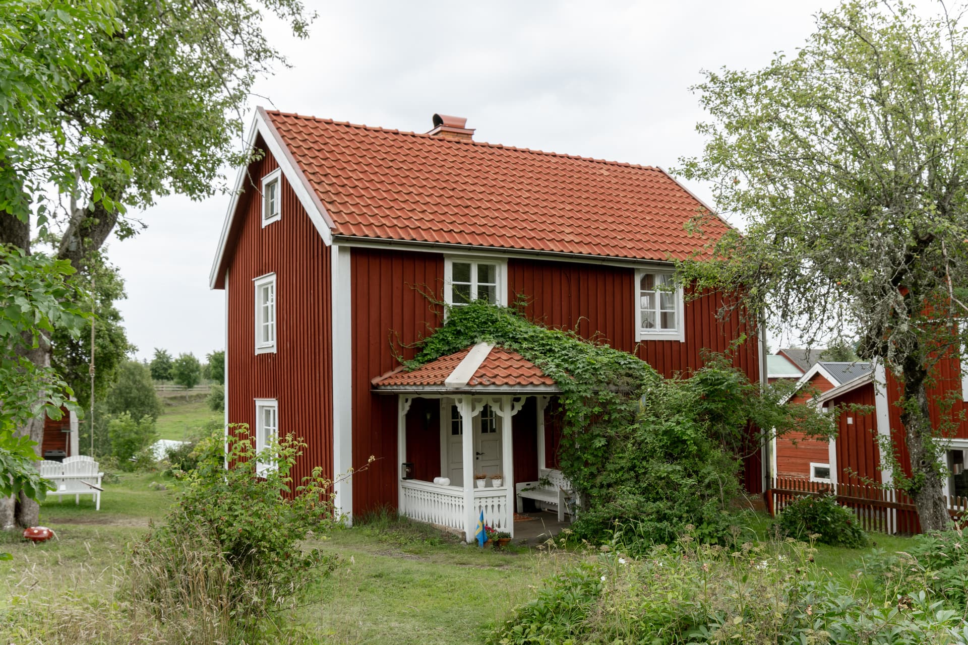 Rött trähus med vit veranda och grönskande trädgård